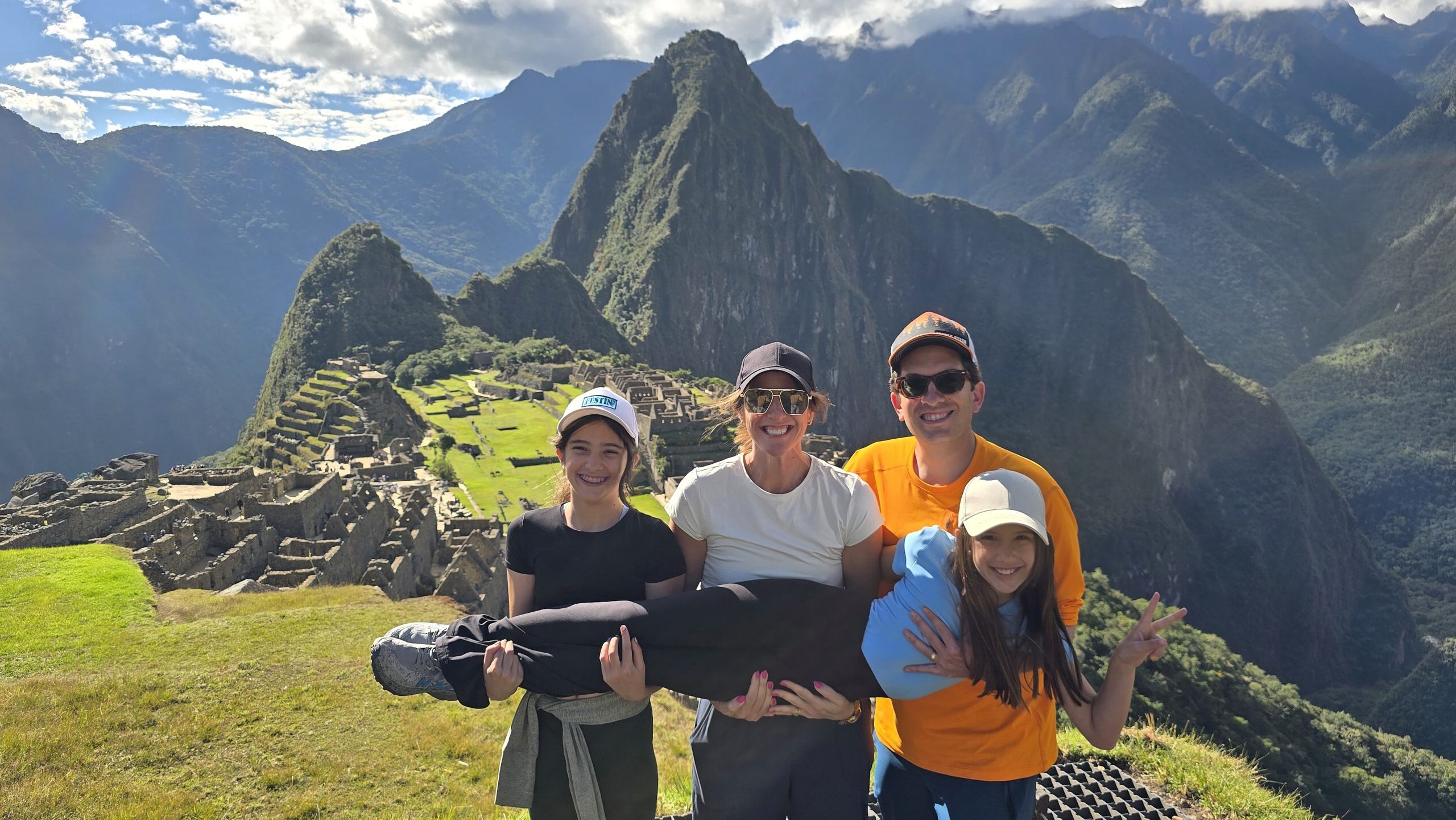 Una familia juega frente a Machu Picchu y sostiene en brazos a la niña más pequeña. Detrás se ven las terrazas de la ciudadela y el Huayna Picchu.